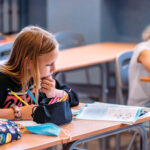 Dziewczynka podczas lekcji. Trzyma ołówek w ręku, zastanawia się nad zadaniem.