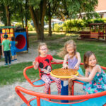 Trzy dziewczynki w koorowych ubraniach bawią sę na karuzeli na placu zabaw
