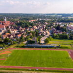 Stadion z bieżnią lekkoatletyczną i trawiastym boiskiem piłkarskim. Na drugim planie widok zabytkowego miasta